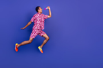 Fototapeta premium Cheerful young man in pink leopard outfit jumping against violet background