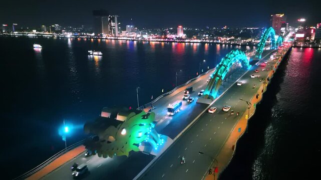 Illuminated dragon bridge spouting fire, casting golden glow across da nang's nighttime skyline, highlighting urban energy alongside han river's shimmering waters