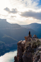 Adventurous woman standing on a rocky cliff, admiring a breathtaking mountain landscape with a shimmering lake in the background. Concept of freedom and exploration. Castillo de Chirel - Valencia