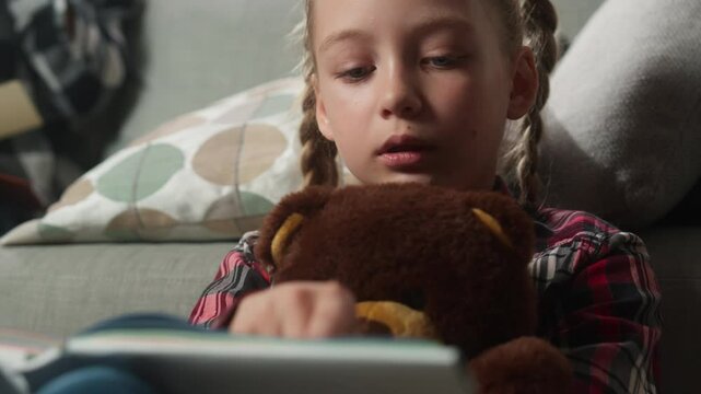 Caucasian pupil teen child kid girl daughter hugging holding toy Teddy bear reading interesting book learning at home studying read novel fairytale education mother working laptop on background family