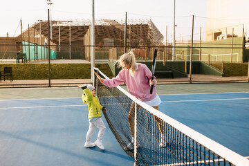 Mother and toddler son playing tennis, giving high five over the net.