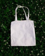 White cotton or mesh bag on green grass with clover flowers background. Zero waste, no plastic, eco...