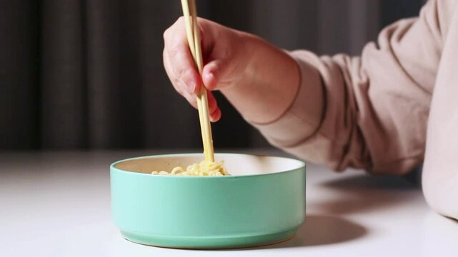 Woman eating ramen noodles with chopsticks from soup bowl at home. Hands taking noodles from bowl. Home made food