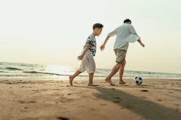 Father and son play football happiness on the beach during vacation, travel, long weekend, summer or any other holiday. They are happy to spend time together.
