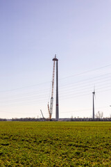 A wind turbine under construction stands next to a fully assembled one, symbolizing progress in renewable energy. The scene captures the transition to sustainable power as the nacelle is being lifted 