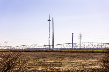 A wind turbine under construction stands next to a fully assembled one, symbolizing progress in renewable energy. The scene captures the transition to sustainable power as the nacelle is being lifted 