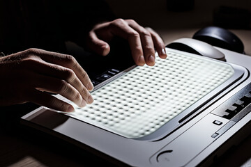 Modern Braille display device connected to a computer, with a visually impaired person using it to read digital text.