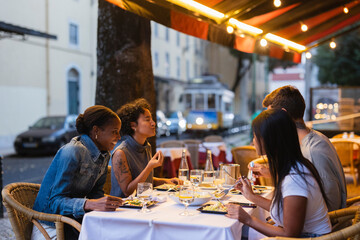Friends enjoying dinner at outdoor restaurant in lisbon with tram passing by