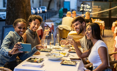 Happy friends taking selfie and toasting with drinks at restaurant