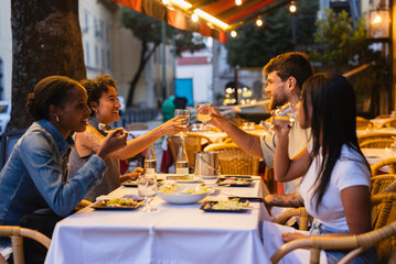 Friends toasting drinks at outdoor restaurant table in the evening