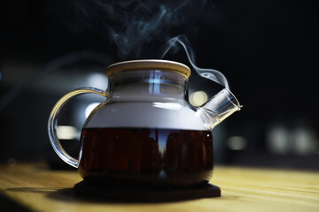 Steaming Glass Teapot with Lid on Wooden Surface in Dimly Lit Cafe