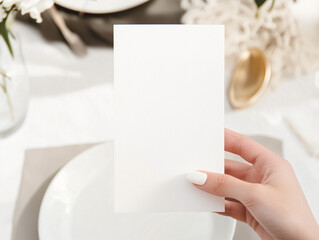 Obraz premium Elegant Presentation: A close-up view of a hand delicately holding a blank card amidst a sophisticated table setting, hinting at a message or invitation in a refined ambiance.