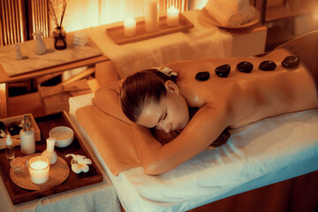Hot stone massage at spa salon in luxury resort with warm candle light, blissful woman customer...
