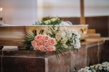 A bouquet of pink roses rests on a wooden coffin, surrounded by white flowers, in a solemn funeral...