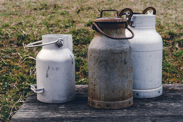 Obraz premium Collection of vintage milk containers displayed on a wooden table in a countryside setting during daylight hours