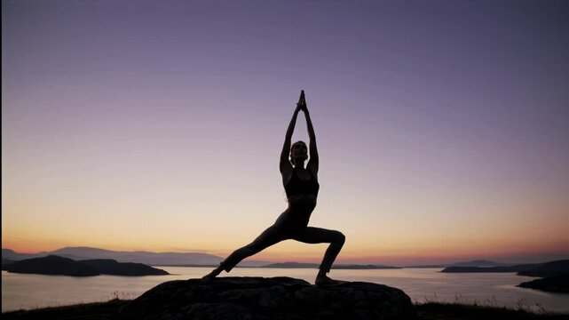 Silhouette of a person in a yoga pose on a hilltop at sunset, captured from a low angle, creating a serene and meditative video scene.