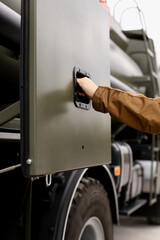 A hand opens the side compartment of a large diesel fueling truck
