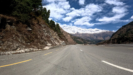 Fototapeta premium Driving down an empty road with a view of mountains in the distance and cloudy sky. 