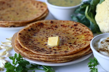 Gobi parathas served with masala raita and dal curry in bowls