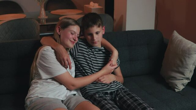 Brother and sister sitting on comfortable sofa in their living room, embracing each other affectionately, creating a heartwarming scene of sibling bonding