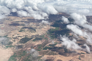 Aerial view of winding river through a desert landscape. Clouds seen from above background. Valley of greenery along the water. Scenic top view perspective from an airplane window. Green river canyon.