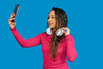 Happy latin woman taking selfie with smartphone while adjusting her headphones