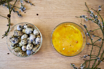 top view of quail eggs and yolks in glass bowls on a wooden table with willow branches, Easter background