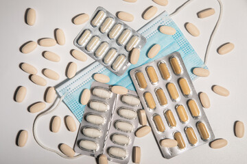Various blister packs with tablets, capsules and medical mask scattered on a light background