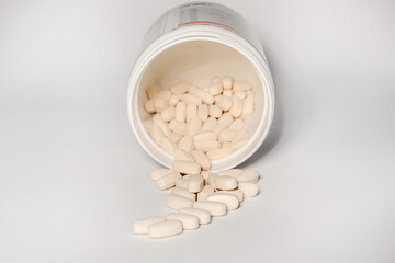 Tablets of vitamins and amino acids on a light table poured out of a large jar