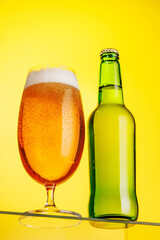 A tall glass of beer with a golden hue and frothy head, on a yellow background