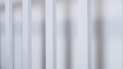 Fototapeta premium Iron rods with white wall background. Texture background of clean rod indoors with shadow. Concept of metal, hard object, material for interior, pipe, and equipment. Close-up straight steel rods.