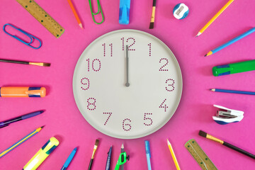 Clock showing noon and stationery on pink background. white round clock surrounded by pens, pencils, markers, and brushes as symbol sun rays for workspace organization, midday break, exam