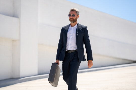 Business outdoor portrait. Businessman walking outdoors. Corporate leader on move. Man in suit with briefcase. Businessman going to work. Urban businessman with briefcase. Businessman go to office.