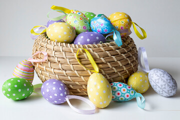 Colorful Easter eggs in a brown wicker basket on a white background. Eggs around the basket and inside. Easter