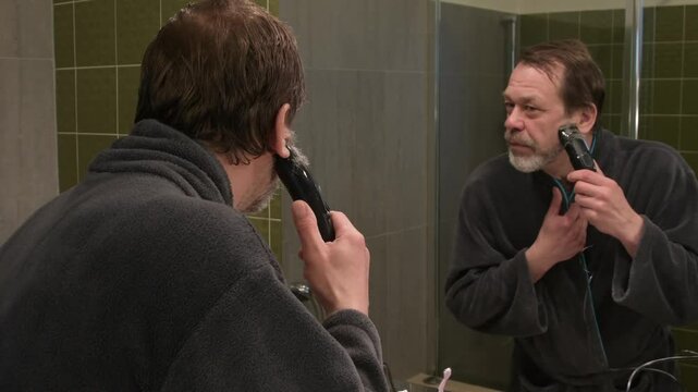 a grown man looks in the mirror and carefully shav