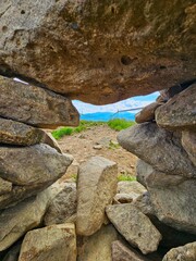 Stone archway framing a hiking trail in Bieszczady, Poland, with grassy path and distant mountains under a cloudy sky
