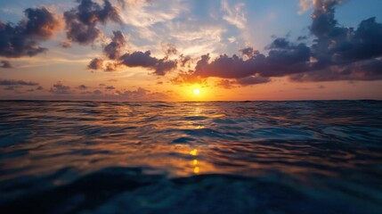 Fototapeta premium A stunning sunset over calm waters, with clouds reflecting vibrant hues of orange and blue, creating a serene and picturesque seascape.
