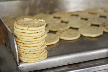 Stack of Traditional Arepas Cooking on a Griddle. Tortillas being prepared on a grill for a street food market. Traditional local cuisine of Latina America. Corn flat bread