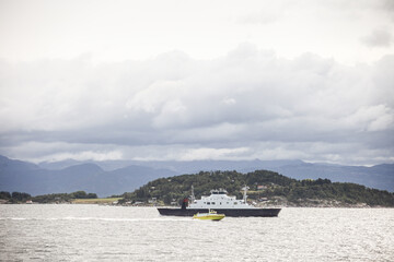 A large ship is sailing in the fjord Norway with a smaller boat in the water