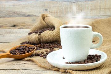 Opened burlap bags, a cup of coffee, scattered whole coffee beans on a white background.