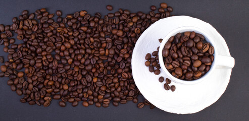 A pile of coffee beans, a white cup of coffee on a dark background. Top view. banner