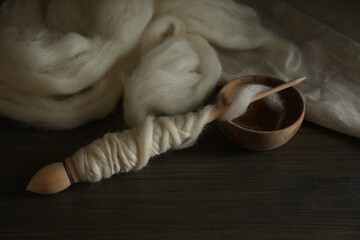 Soft white wool and spindle on wooden table