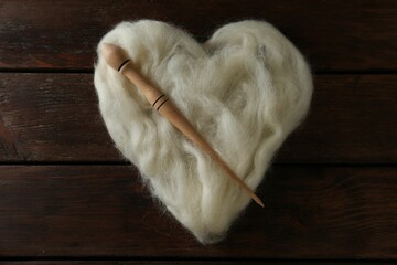 Heart shaped pile of white wool and spindle on wooden table, top view