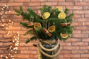 Beautiful fir tree branches decorated with dried orange slices and cinnamon sticks in vase against Christmas lights