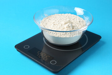 Electronic kitchen scale with flour on light blue background, closeup