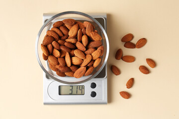 Electronic kitchen scale with almonds on beige background, top view
