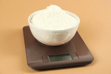 Electronic kitchen scale with bowl of flour on beige background, closeup