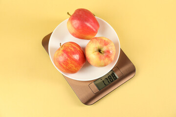 Electronic kitchen scale with apples on yellow background, top view