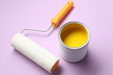 Can of yellow paint and roller on violet background