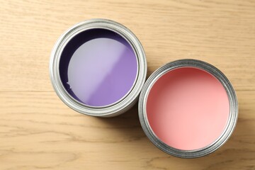 Cans of violet and pink paints on wooden background, flat lay